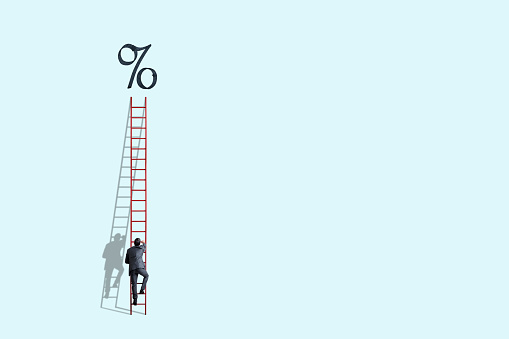 A man  climbs a tall read ladder leading to higher interest rates.