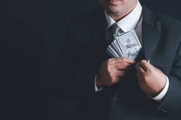 Photo of Man putting bribe money into pocket on black background,
