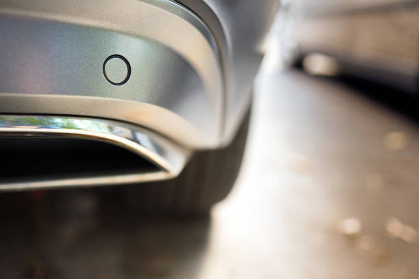 istock Selective focus on rear bumper parking sensor near exhaust pipe at back of luxurious car bumper close up near other car on light blurred with sun flare background with copyspace. 1307120062