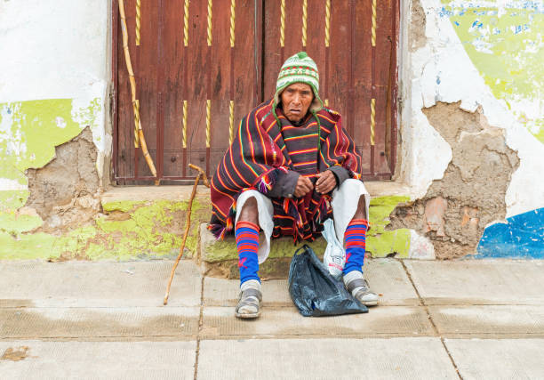 Indigenous Tarabuco man in traditional clothing sitting in front of a wooden door, Tarabuco town, Sucre region, Bolivia.