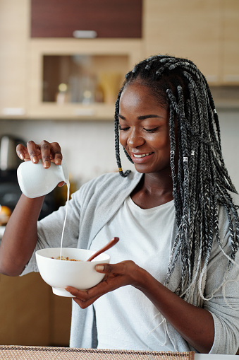 Portrait of smiling beautiful young woman adding fresh non-dairy milk in bowl of cereals