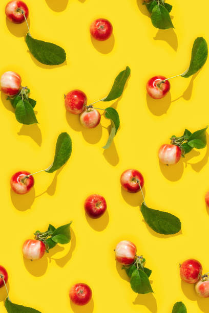 istock Regular creative pattern from ripe small red apples and green leaves on yellow color background. 1307128702