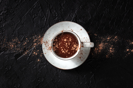 Hot chocolate with ground cocoa powder, overhead shot on a black background