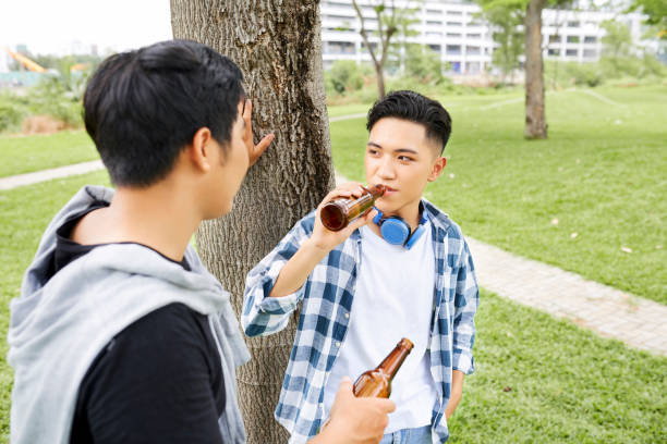 Two teenage boys drinking beer from bottles together while standing outdoors