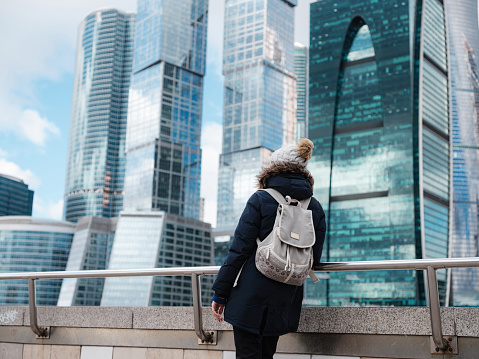 Young beautiful woman and Moscow City international business center in the background. Cold Winter day. Travel to Russia