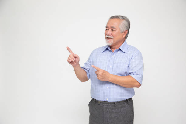 istock Senior Asian man smiling and pointing to empty copy space isolated on white background 1307139928