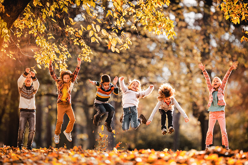 Group of playful kids having fun while jumping during autumn day in nature.