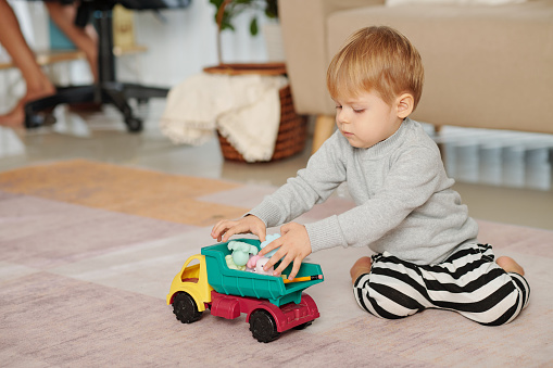 Little boy sitting on the floor and playing with his toy car in the room