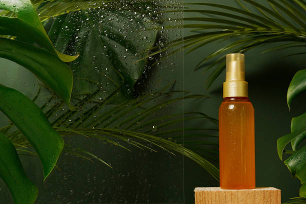 gesichtsserum flüssigkeitskosmetisches öl in der flasche mit frische grünen tropischen blättern und wassertropfen auf grünem hintergrund. eco bio natürliche schönheit hautpflege produkt. dermatologie und kosmetologie - gold leaf fotos stock-fotos und bilder