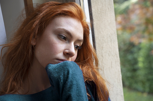 Young Asian woman sitting alone in bedroom, feeling bad and unhappy while thinking about her problems, representing failure, lost love, depression. Dark and moody, negative emotions.