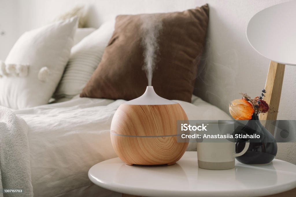 Aroma oil diffuser on chair against in the bedroom. Aromatherapy Concept. Aroma oil diffuser on chair against in the bedroom. Air freshener. Ultrasonic aroma diffuser for home Aromatherapy Diffuser Stock Photo