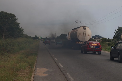 Agbantokopé, Togo - October 22, 2018: Air pollution from the exhaust of a truck. Black smoke obstructs the view of motorcyclists and motorists.