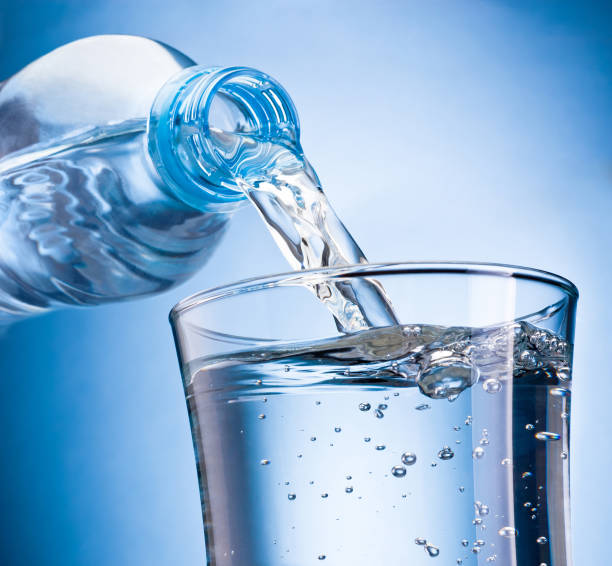 wasser aus plastikflasche in glas auf blauem hintergrund isoliert gegossen - gurgling stock-fotos und bilder