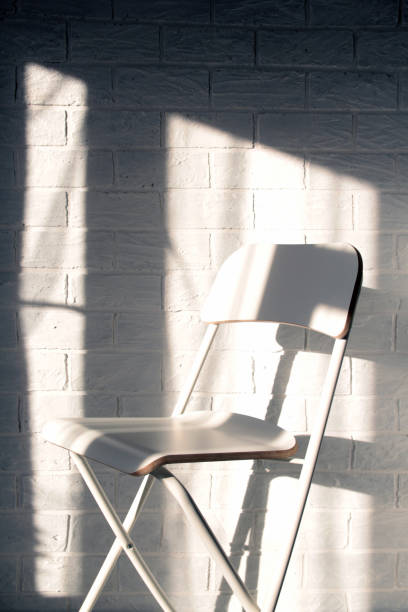 istock One white chair against a brick wall and light from a window with a shadow 1307159039