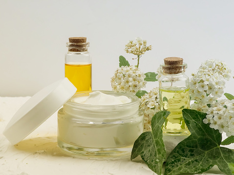 Closeup shot of organic oil and cream. green cosmetic arrangement, Fresh herbal skincare cosmetics. Essential oil, craft bottle, flowers, jar facial cream. Natural beauty care remedy