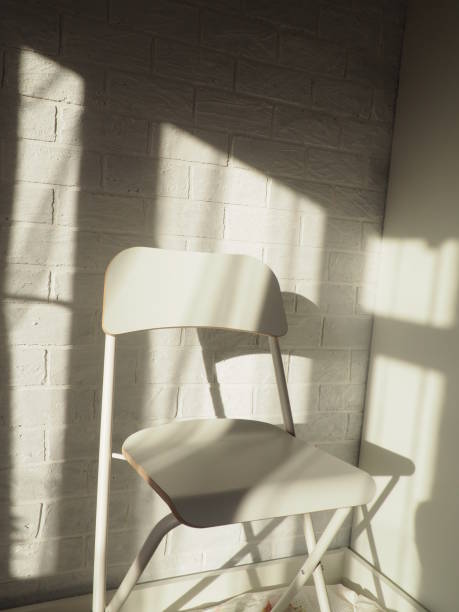 istock One white chair against a brick wall and light from a window with a shadow 1307159062
