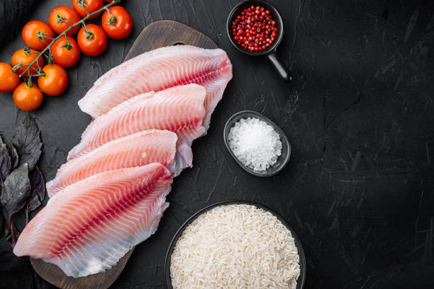 生の白身魚ティラピア、バスマティライスとチェリートマトの材料、黒の背景、トップビュー - prepared fish tilapia fillet seafood ストックフォトと画像