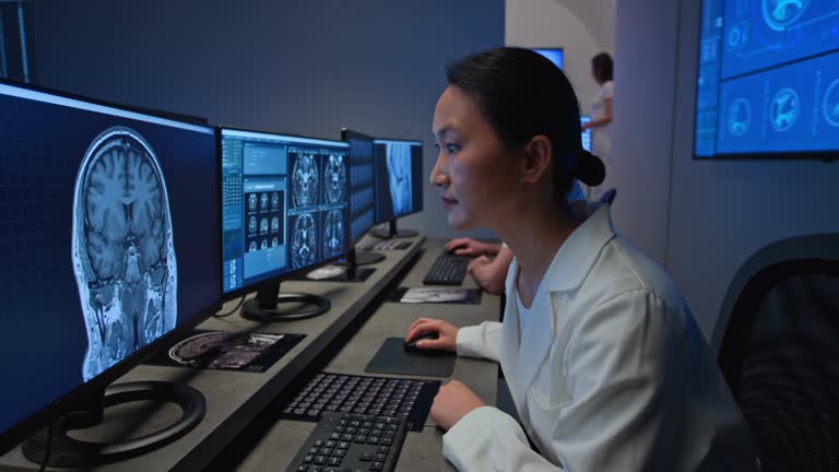 Wide dolly shot of an Asian female radiologist analysing a head MRI scan on her computer alongside her male colleague. Shot in Slovenia.