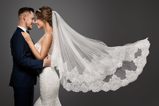 Wedding Couple Dancing. Romantic Bride and Groom Portrait. Bridal long Veil flying on Wind in Air over Black Studio Background