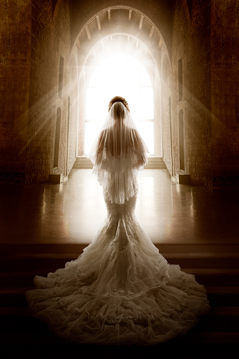 Bride Back Side View walking down Aisle Church in Light. Wedding Ceremony Day. Bridal Dress long Train and Lace Veil. Indoor Art Portrait in front Shining Window Door
