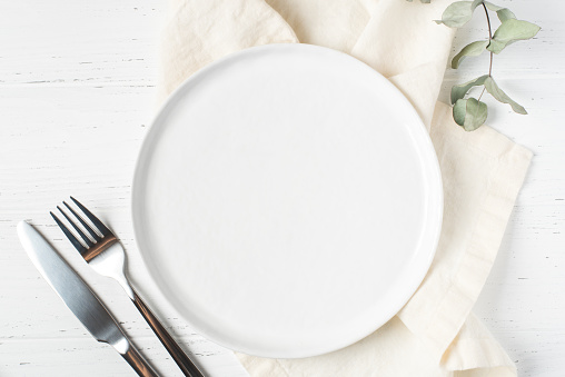 An empty plate and cutlery on a white table.