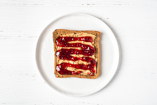 Homemade peanut butter sandwich with raspberry jam on wooden background.