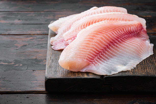 生のティラピア魚のフィレ肉、暗い木製の背景に - prepared fish tilapia fillet seafood ストックフォトと画像