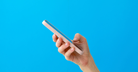Close-up of silhouette of woman hands using smartphone touchscreen on blue background. Side view palms shadow typing message on mobile phone blue background
