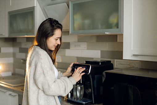 The young beautiful woman choose coffee to prepare in the coffee machine at home in the morning