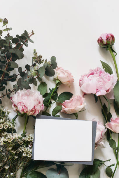 istock Spring, summer wedding still life scene Floral composition. Blank greeting card mockup. Pink roses, peonies flowers and eucalyptus branches isolated on white wooden background. Flat lay, top view. 1307161746
