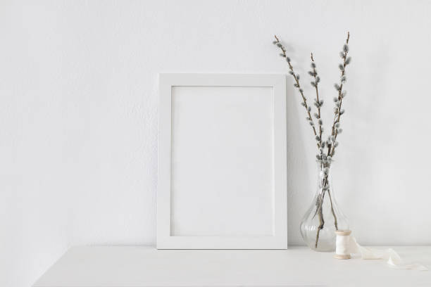 istock Easter spring still life. Blank vertical picture frame mockup on white wooden table. Blooming pussy willow branches with catkins in glass vase. Art concept. Scandinavian interior design, no people. 1307161776