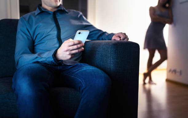 Jealous woman and cheating man with a phone. Infidelity, jealousy and betrayal. Cheater husband texting with mistress and secret lover. Suspicious wife peeking and spying. stock photo