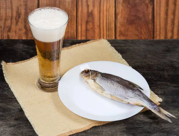 Photo of Dried roach fish and glass of beer on dark table