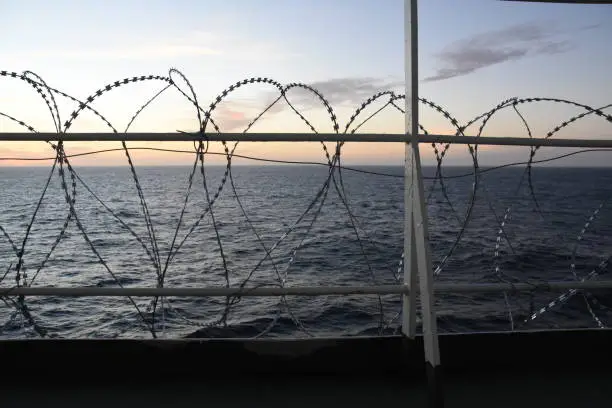 Photo of Barbed wire attached to the ship hull, superstructure and railings to protect the crew against piracy attack in the Gulf of Guinea in West Africa sailing during sunset.