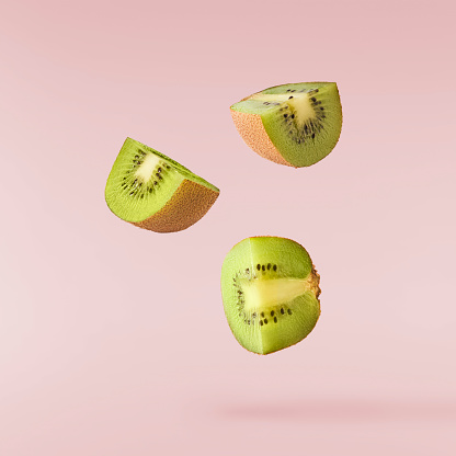 Fresh raw kiwi falling in the air isolated on pink background. Food levitation concept. High resolution image