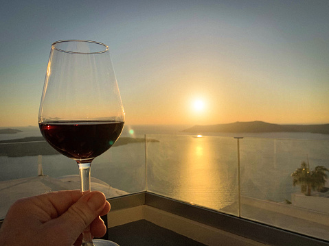 Wine glasses with red wine at sunset, view from idyllic village Firostefani on Santorini island, Greece. Property released.