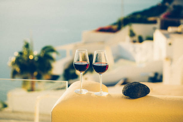 Wine glasses with red wine at sunset, view from idyllic village Firostefani on Santorini island, Greece. Property released.
