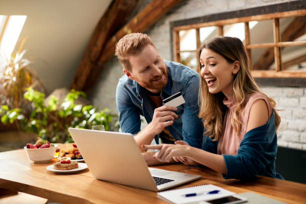 Happy couple having fun while online shopping at home. Happy woman pointing on something on laptop screen while shopping on the internet with her husband at home. spending money stock pictures, royalty-free photos & images