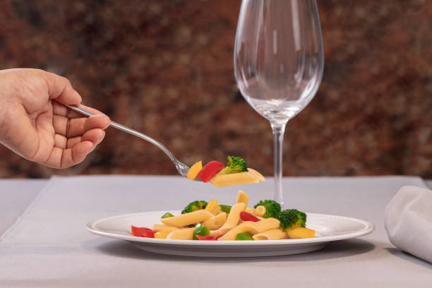 istock a fork with pasta and vegetables held by a hand over a plate of pasta salad 1307185567