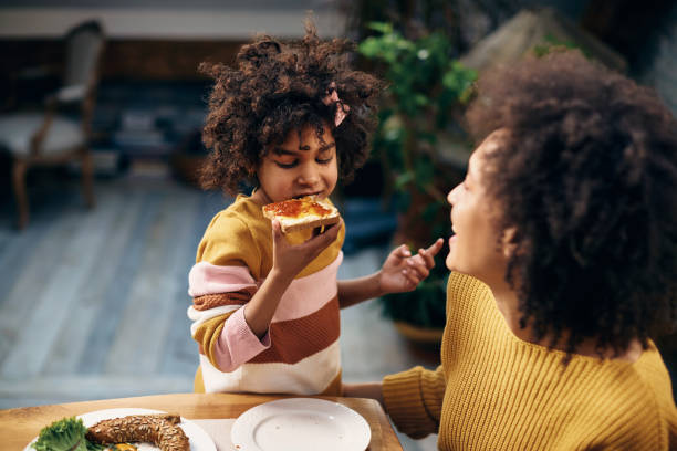 Small black girl eating toasted bread with jam for breakfast.