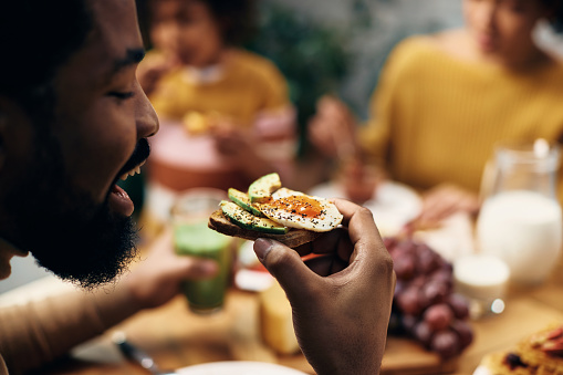 Close-up of African American man eating sandwich with avocado and eggs.