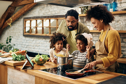 Happy African American parents and their kids making family meal in the kitchen.