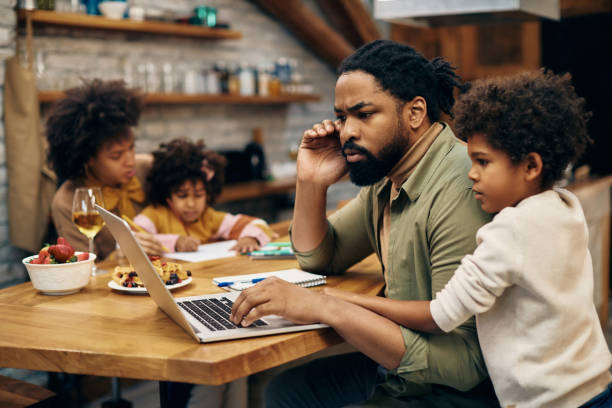 istock Pensive black father working on computer while being with his family at home. 1307187925