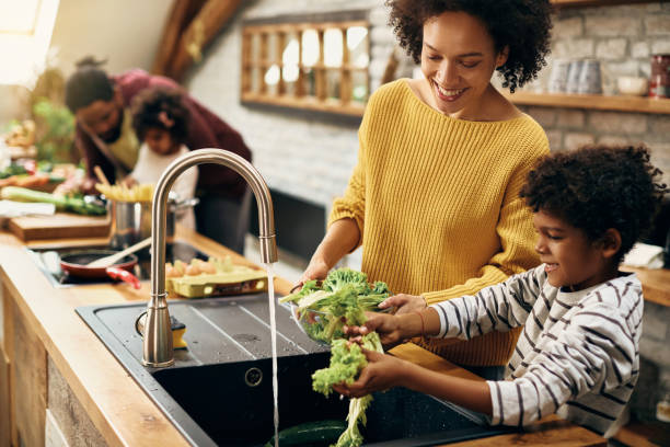 キッチンで食べ物を準備しながらサラダを見て幸せな黒い母と息子。 - mother son family cooking ストックフォトと画像