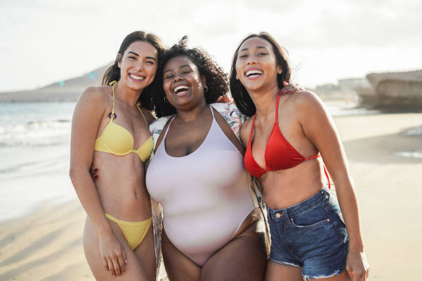 mujeres multirraciales felices con diferentes cuerpos y pieles divirtiéndose en el día de verano en la playa - enfoque principal en la cara de la chica central - beach body fotografías e imágenes de stock