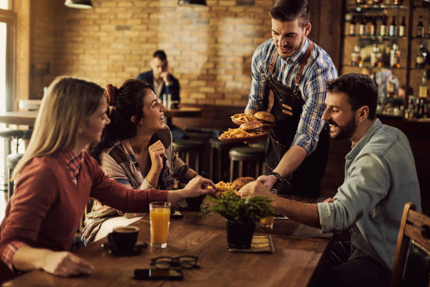 happy waiter serving food to group of friends in a pub. - restaurant imagens e fotografias de stock