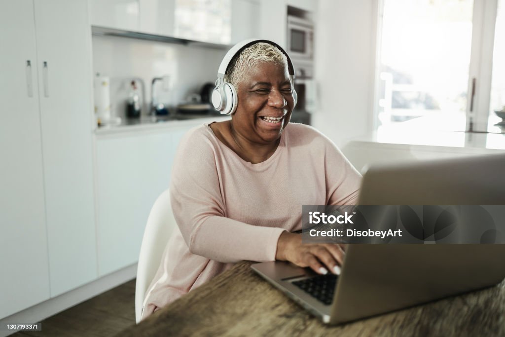 Senior woman using laptop while wearing headphones at home - Joyful elderly lifestyle and technology concept - Focus on face Senior Adult Stock Photo