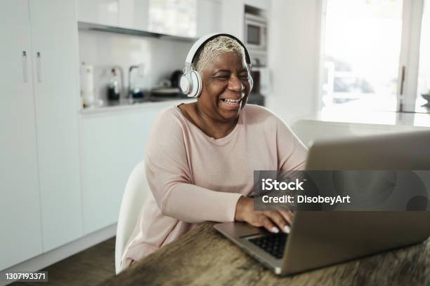 Senior Woman Using Laptop While Wearing Headphones At Home Joyful Elderly Lifestyle And Technology Concept Focus On Face Stock Photo - Download Image Now