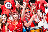 Football supporter fans cheering with confetti watching soccer match cup at stadium tribune - Young people group with red t-shirt having excited fun on sport world championship - Bright vivid filter