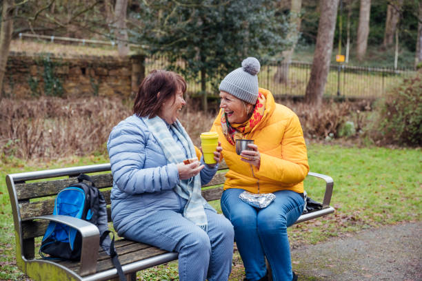 Homemade Cafe Two senior women on a walk together in the North East of England. They are sitting on a park bench drinking tea from an insulated drink container. senior adult women park bench 70s stock pictures, royalty-free photos & images